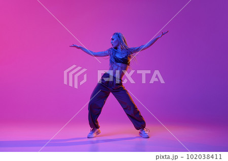 Stylish sporty girl, modern dancer moving to the beat of music over purple studio background in neon light. Freedom 102038411