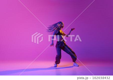 Portrait with young adorable girl with flying hair dancing over gradient purple background in neon light. Solo performance 102038432