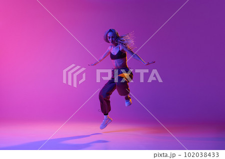 One dancer, woman wearing casual clothes jumping up in motion over gradient purple neon background. Improvisation 102038433