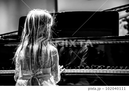 Blonde young Caucasian girl child in a dress playing a piano at a recital.  102040111