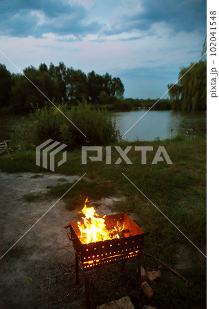 evening-burning firewood in the grill, preparation for the frying of meat, near the lake evening-burning firewood in the grill, preparation for the frying of meat, near the lake 102041548