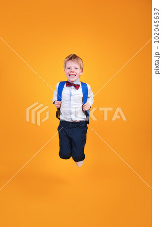 Funny school boy with a backpack jumping on yellow studio background 102045637