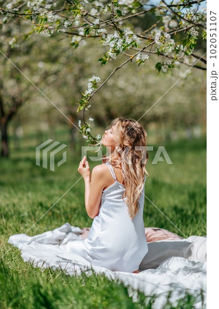 woman sleeps on a white bed in the fresh spring grass in the garden. Dressed in a blue nightgown. woman sleeps on a white bed in the fresh spring grass in the garden. Dressed in a blue nightgown. 102051107
