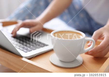 Woman taking cup of morning coffee while working on laptop indoors, closeup Woman taking cup of morning coffee while working on laptop indoors, closeup 102053915