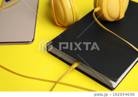 Book, modern headphones and smartphone on yellow background, closeup Book, modern headphones and smartphone on yellow background, closeup 102054030