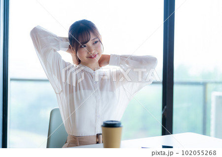 緑を望むオフィスの窓辺でストレッチしてリフレッシュする若い女性ワーカー 102055268