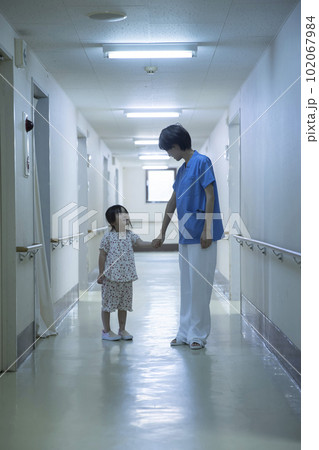 病院の廊下で女の子の患者と手を繋ぐ看護師 102067984