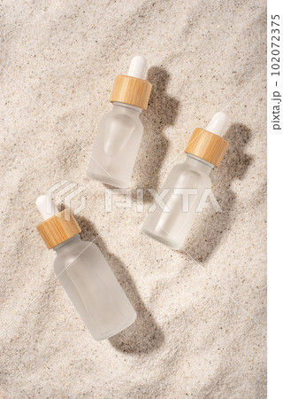 Glass bottles with a cosmetic product on a natural sandy background. Top view. Glass bottles with a cosmetic product on a natural sandy background. Top view. 102072375