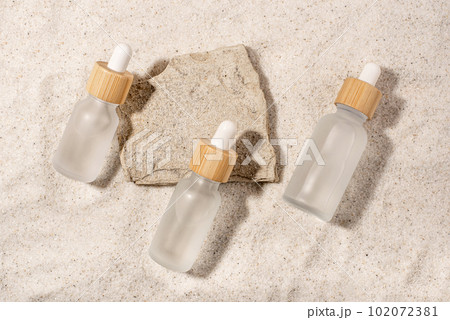 Glass bottles with a cosmetic product on a natural sandy background. Top view. 102072381