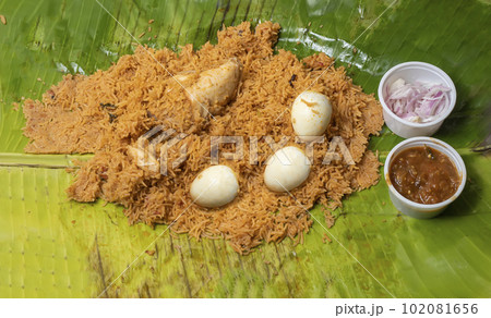 Chicken biryani served with raita and onions on a banana leaf. Chicken biryani served with raita and onions on a banana leaf. 102081656