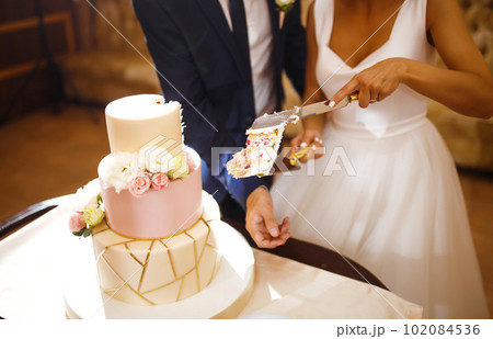 Happy bride and a groom is cutting their stylish wedding cake on wedding banquet. Sweet cake for couple. 102084536