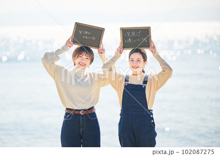 海でブラックボードを頭の上に掲げる若い女性と友達 102087275