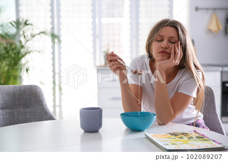 Sleepy young woman eating breakfast at home in morning 102089207