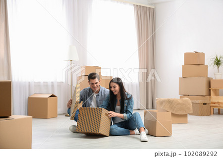 Happy couple unpacking cardboard boxes in their new flat on moving day 102089292
