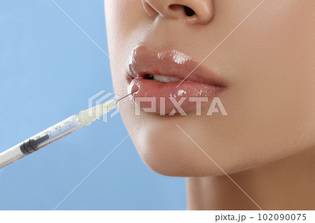 Young woman getting lips injection on light blue background, closeup Young woman getting lips injection on light blue background, closeup 102090075