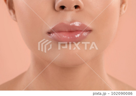 Young woman with beautiful full lips on peach background, closeup 102090086