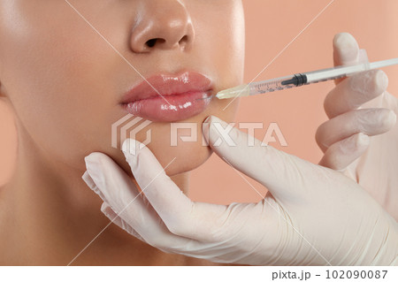 Young woman getting lips injection on peach background, closeup Young woman getting lips injection on peach background, closeup 102090087