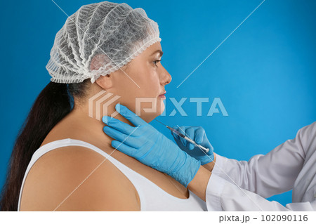 Woman with double chin getting injection on blue background. Cosmetic surgery Woman with double chin getting injection on blue background. Cosmetic surgery 102090116