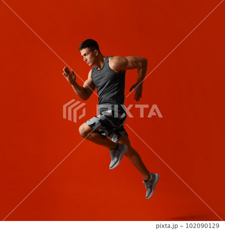 Athletic young man running on red background, side view Athletic young man running on red background, side view 102090129