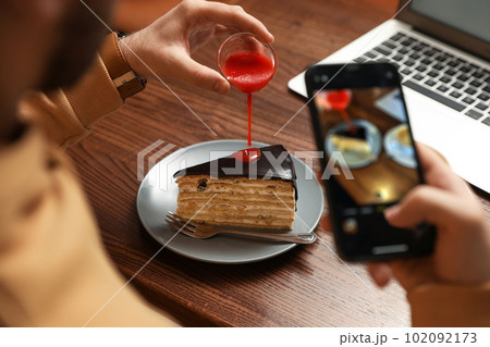 Male blogger taking photo of dessert at table in cafe, closeup Male blogger taking photo of dessert at table in cafe, closeup 102092173