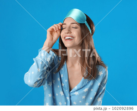 Beautiful woman wearing pajamas and sleep mask on light blue background. Bedtime Beautiful woman wearing pajamas and sleep mask on light blue background. Bedtime 102092896