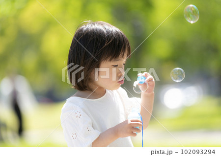 新緑の初夏の公園でシャボン玉をして遊ぶ小さな女の子 102093294