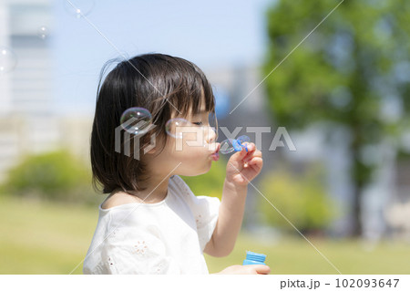新緑の初夏の公園でシャボン玉をして遊ぶ小さな女の子 102093647