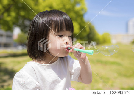 新緑の初夏の公園でシャボン玉をして遊ぶ小さな女の子 102093670