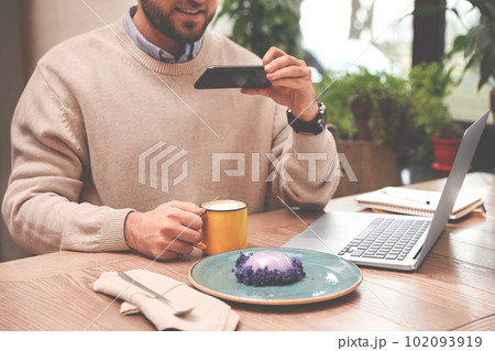 Male blogger taking photo of dessert and coffee at table in cafe, closeup 102093919