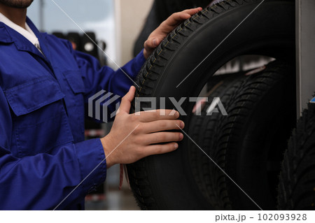 Male mechanic with car tire in auto store, closeup Male mechanic with car tire in auto store, closeup 102093928