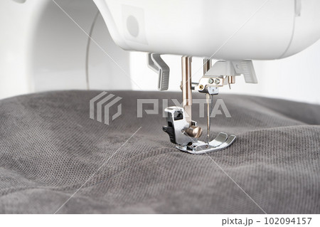 Modern sewing machine presser foot with gray fabric and thread, closeup Modern sewing machine presser foot with gray fabric and thread, closeup 102094157