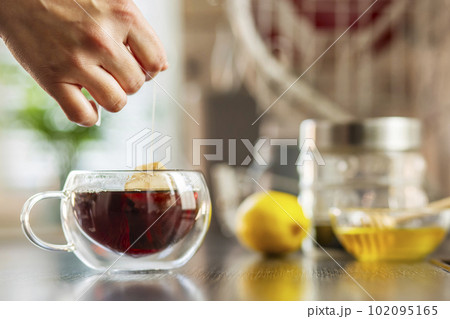 Woman puts the tea bag in the glass cup with hot water 102095165