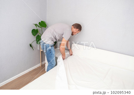 A man makes his cozy bed with fresh bright white A man makes his cozy bed with fresh bright white 102095340