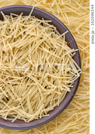 Egg noodles, pasta, in a brown ceramic bowl and scattered around isolated on white background 102096544