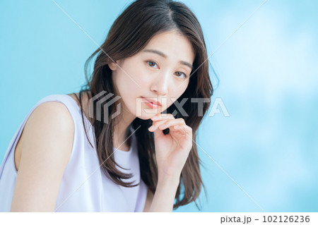 日差しが差し込むブルーバックでスキンケアをする若い女性 102126236