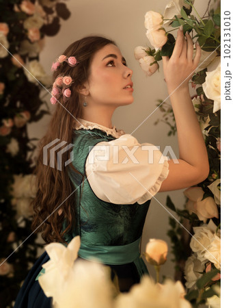 A young peasant woman standing in a garden with flowers dressed in a 19th century bavarian dress. A young peasant woman standing in a garden with flowers dressed in a 19th century bavarian dress. 102131010