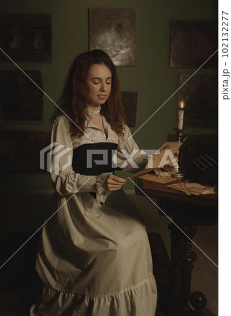 Beautiful woman in vintage clothes reading a letter by candlelight in an art studio 102132277