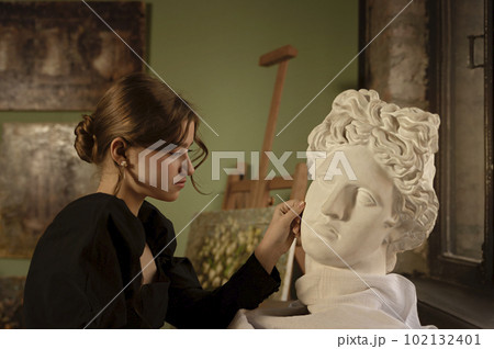 A young girl sits at a table near the bust and touch it. 102132401