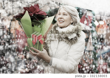 Mature woman in tinsel with Christmas flowers at fair 102138003