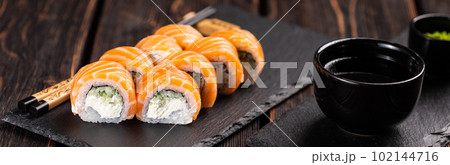 Banner Sushi roll philadelphia with salmon and cucumber and cream cheese on black background close-up. Sushi menu. Japanese food concept Banner Sushi roll philadelphia with salmon and cucumber and cream cheese on black background close-up. Sushi menu. Japanese food concept 102144716