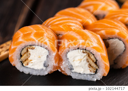 Close up Sushi roll philadelphia with salmon and eel and cream cheese on black background close-up. Sushi menu. Japanese food concept Close up Sushi roll philadelphia with salmon and eel and cream cheese on black background close-up. Sushi menu. Japanese food concept 102144717