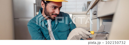 Smiling professional worker in uniform is assembling furniture on kitchen. Repair concept Smiling professional worker in uniform is assembling furniture on kitchen. Repair concept 102150732