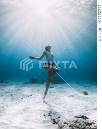Freediver underwater. Freediving with woman in blue ocean with sandy bottom and sun rays 102152743