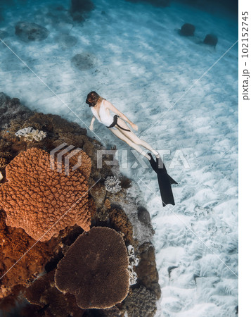 Freediver woman glides on the deep with fins near corals in tropical sea 102152745