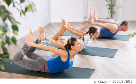 Happy middle-aged woman practicing bow pose of yoga with her family 102153608
