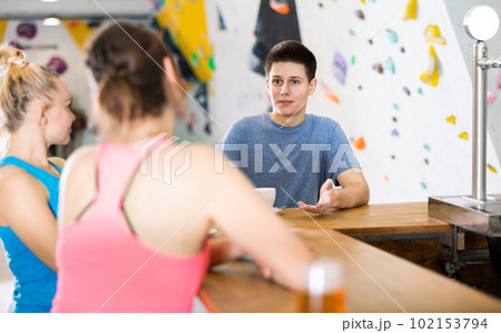 Two sports women and a guy communicate after training on a climbing wall at a table in cafe 102153794