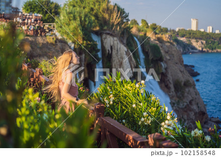 Beautiful woman with long hair on the background of Duden waterfall in Antalya. Famous places of Turkey. Lower Duden Falls drop off a rocky cliff falling from about 40 m into the Mediterranean Sea in 102158548