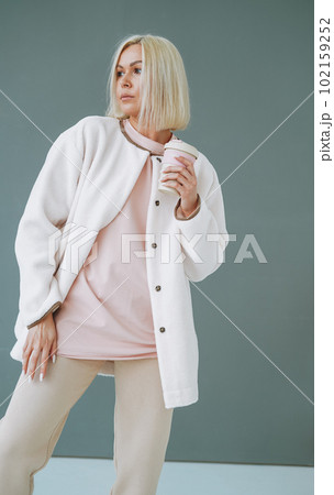 Portrait of young blonde woman in sportswear with thermocup on background of grey wall 102159252