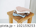 Stack of cotton tops in natural tones on wooden chair in bright room 102159253