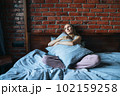 Young adult woman with blonde long hair in casual sitting on bed with pillow at the home 102159258